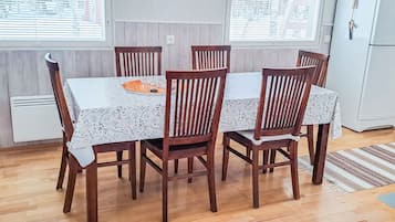 A dining area with a table and six chairs, a window with blinds, a white radiator, and a refrigerator.