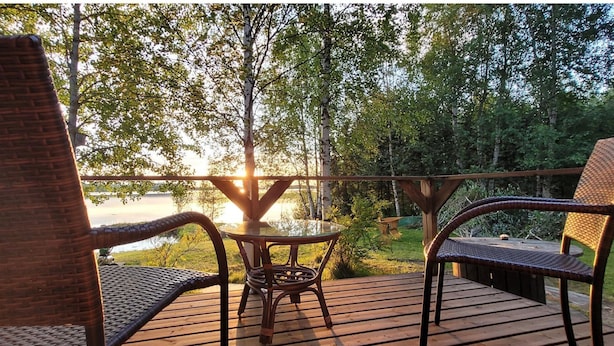 A wooden deck with wicker chairs and a glass table overlooking a lake. - Koivulahden reinola by Interhome (Ylitornio)