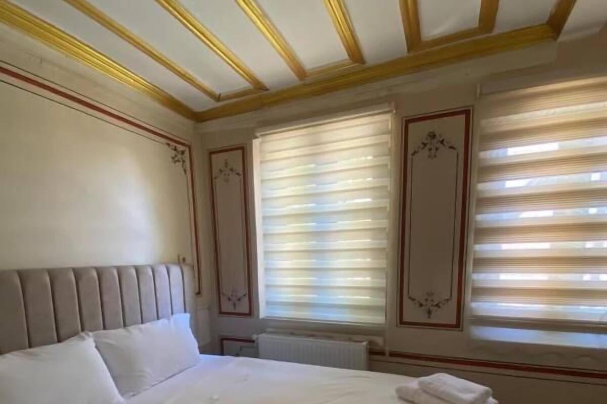 A hotel room with a large bed, a headboard, and a window with blinds.