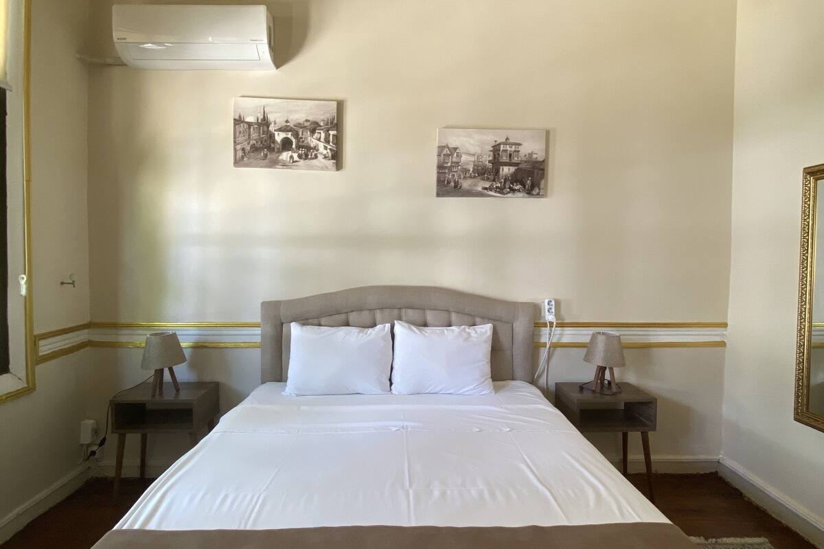 A hotel room with a large bed, two bedside tables with lamps, a ceiling with decorative molding, and two framed pictures on the wall.