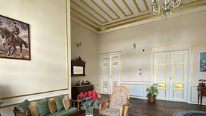 A spacious living room with a wooden floor, a green sofa, a wooden coffee table, a wicker chair, and a blue patterned rug. - Oasis Pansiyon (Edirne)
