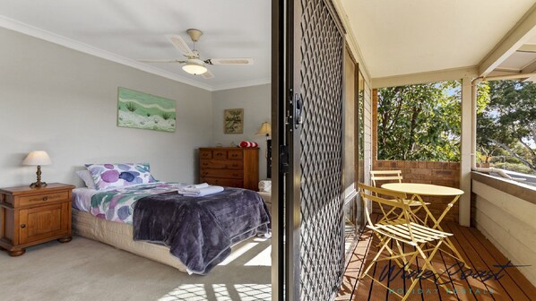Un dormitorio con cama, mesita de noche, cómoda y ventana con vistas a la vegetación.