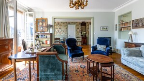 Ein großzügiger Wohnraum mit einer Chandelieber, blauen Sesseln, einem Sofa und einem Essbereich mit Tisch und Stühlen.