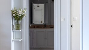 Ein Flur, der zu einem Badezimmer mit weißen Schränken und Holzboden führt.