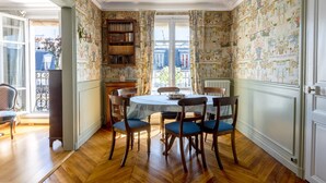 Ein Esszimmer mit einem runden Tisch, vier Stühlen und einem Bücherregal.