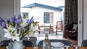 Una mesa de comedor con un florero, una botella y vistas a una casa y un patio.