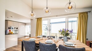 Un comedor moderno con una mesa de madera dispuesta para cuatro personas, sillas tapizadas en gris e iluminación colgante.