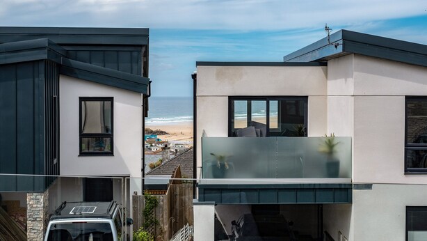Una casa moderna de dos pisos con un balcón que da a la playa.