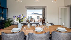 Un comedor con una mesa de madera dispuesta para seis personas, rodeada de sillas tapizadas en gris. Tres lámparas colgantes iluminan la mesa.