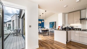 Una cocina moderna con una isla central, un comedor con puerta de vidrio que da a un balcón, y una sala de estar con una pared azul.