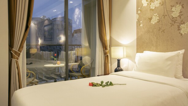 Una habitació d'hotel amb un llit, una taula de nit amb una làmpada, una cadira i vista a través d'una porta de vidre.