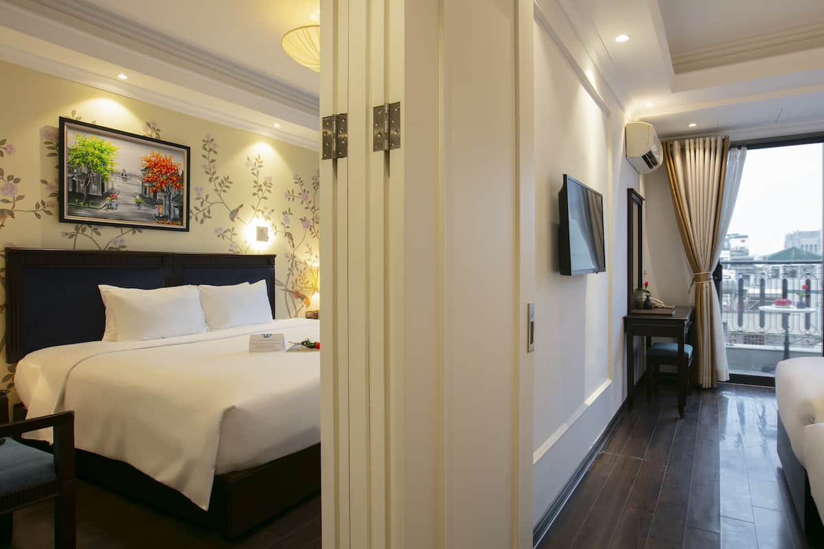 A hotel room with a large bed, a desk, a TV, and a balcony with a view.