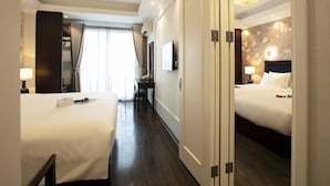 Habitació d'hotel amb dos llits, un escriptori i una cadira. Hi ha un finestral gran amb cortines, un televisor penjat a la paret i un mirall.