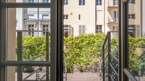 Vista a través de una ventana con barandilla de metal, que da a un edificio con múltiples ventanales y balcones.