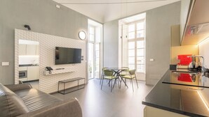 Una sala de estar moderna con un televisor de pantalla plana, un sofá, un comedor con sillas y una cocina con un electrodoméstico rojo.