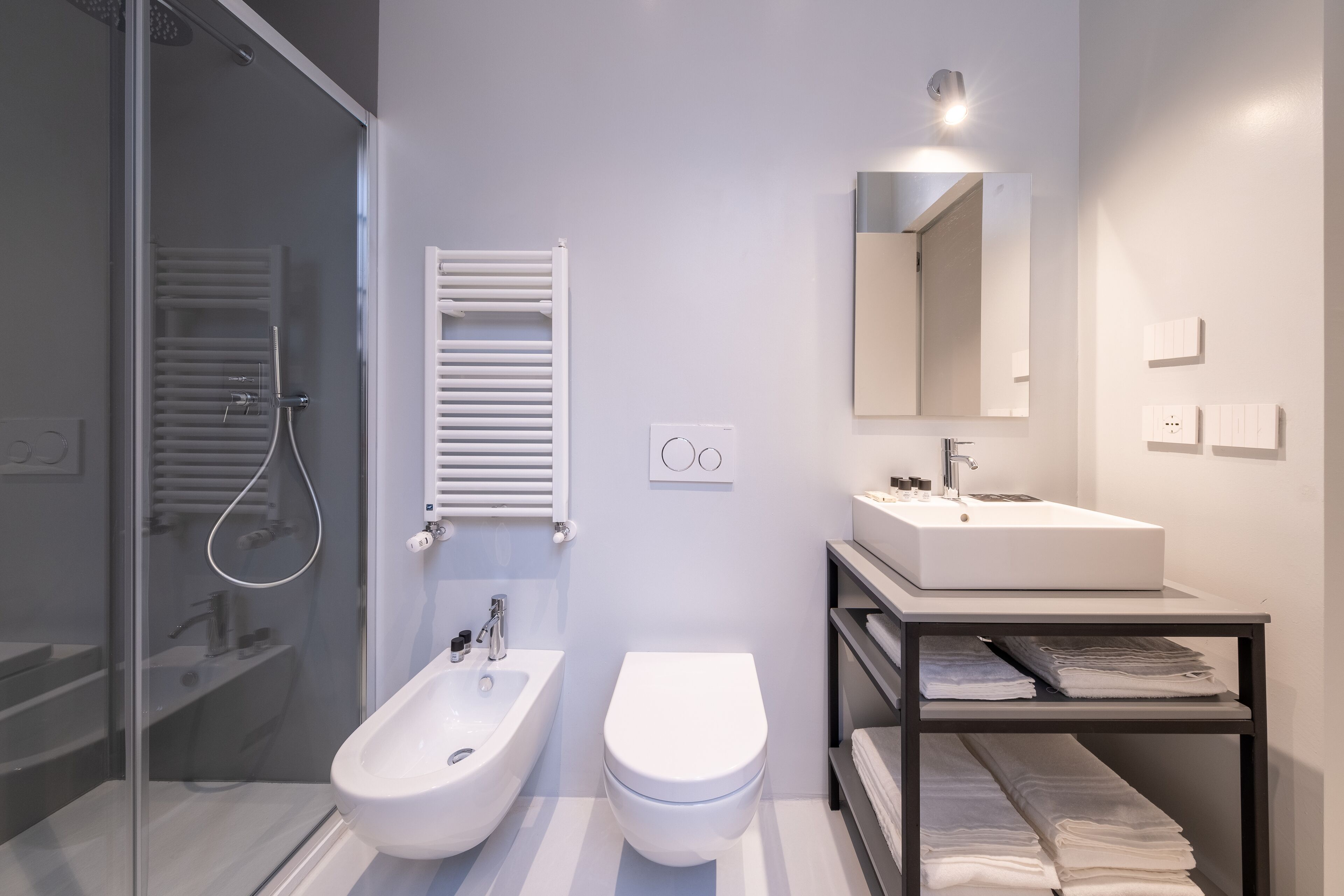 Un baño moderno con cabina de ducha de vidrio, un bidé, un inodoro, un lavamanos y un perchero para toallas.