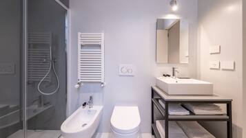 Un baño moderno con cabina de ducha de vidrio, un bidé, un inodoro, un lavamanos y un perchero para toallas.