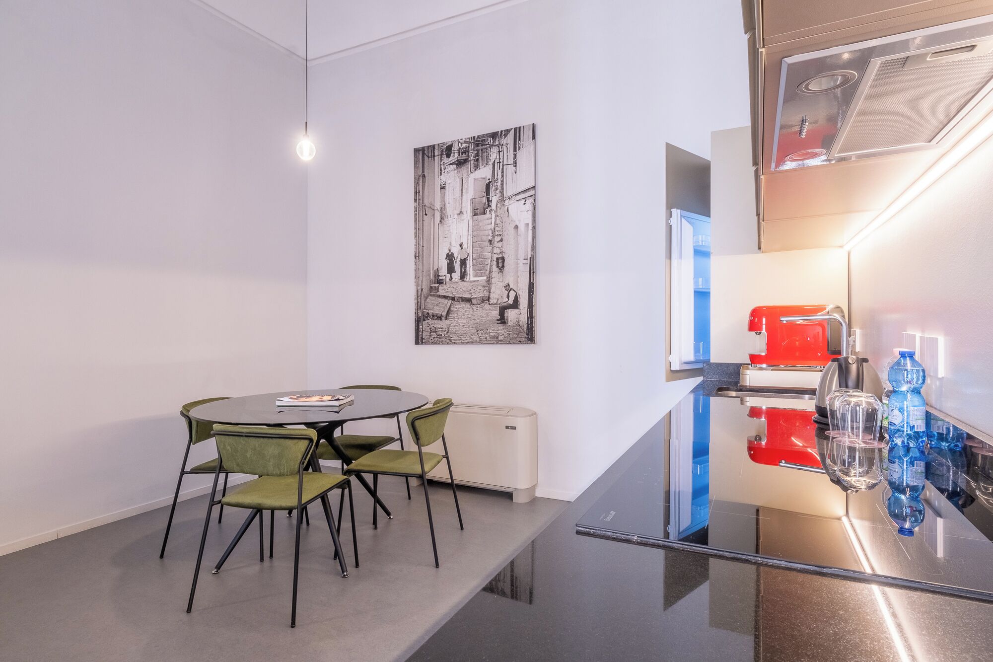 Une cuisine moderne avec une machine à café rouge, un distributeur d’eau en verre et un réfrigérateur en acier inoxydable.