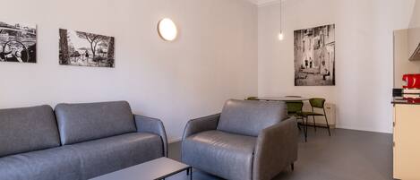A modern living room with a grey sofa, a small table, and two black-and-white photographs on the wall.