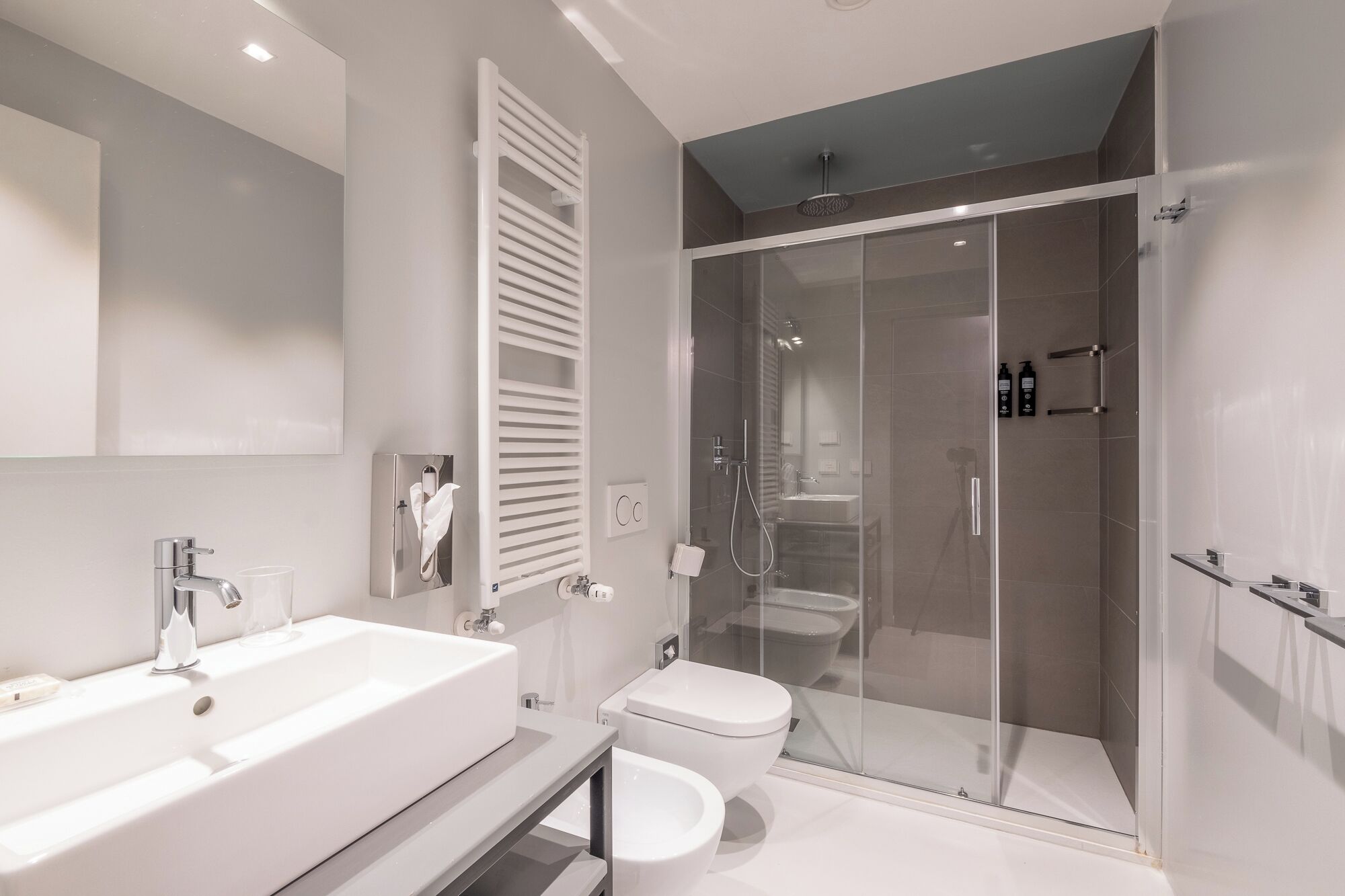 Un baño moderno con un lavabo grande de color blanco, un inodoro y una zona de ducha con mampara de vidrio.