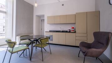 A modern kitchen with a dining area, featuring a round table, green chairs, and a brown armchair.