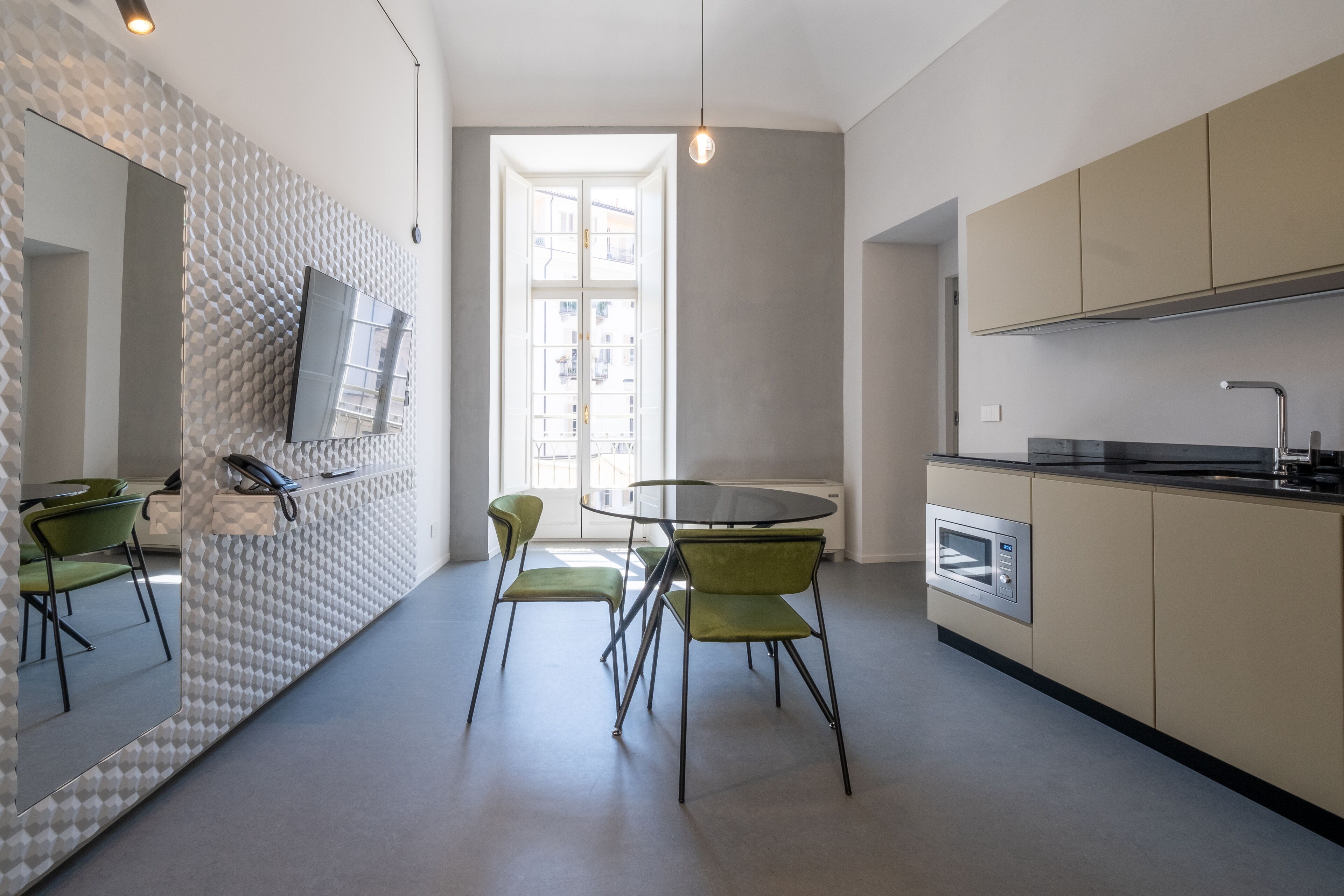 Una cocina moderna con una mesa redonda de vidrio, sillas verdes y un horno empotrado.