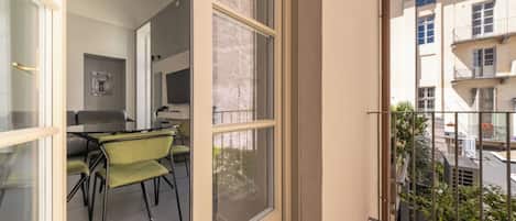 Un appartement moderne doté d’un balcon, d’un coin repas avec des chaises vertes et d’une cuisine visible à travers la fenêtre.