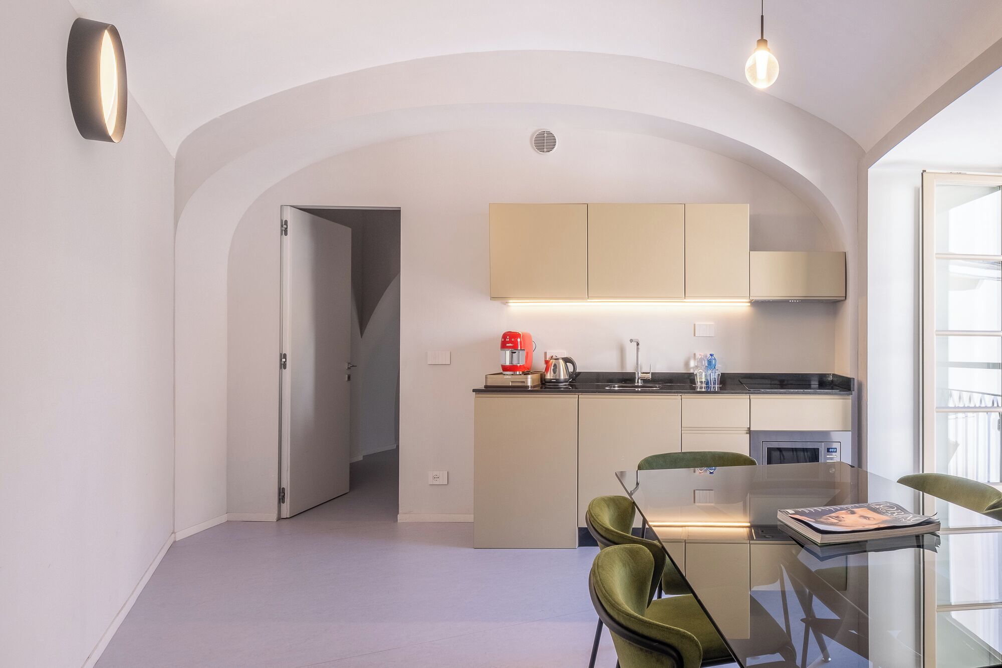 Ett modernt kök med matplats, med ett glasbord och gröna stolar, under ett välvt tak.