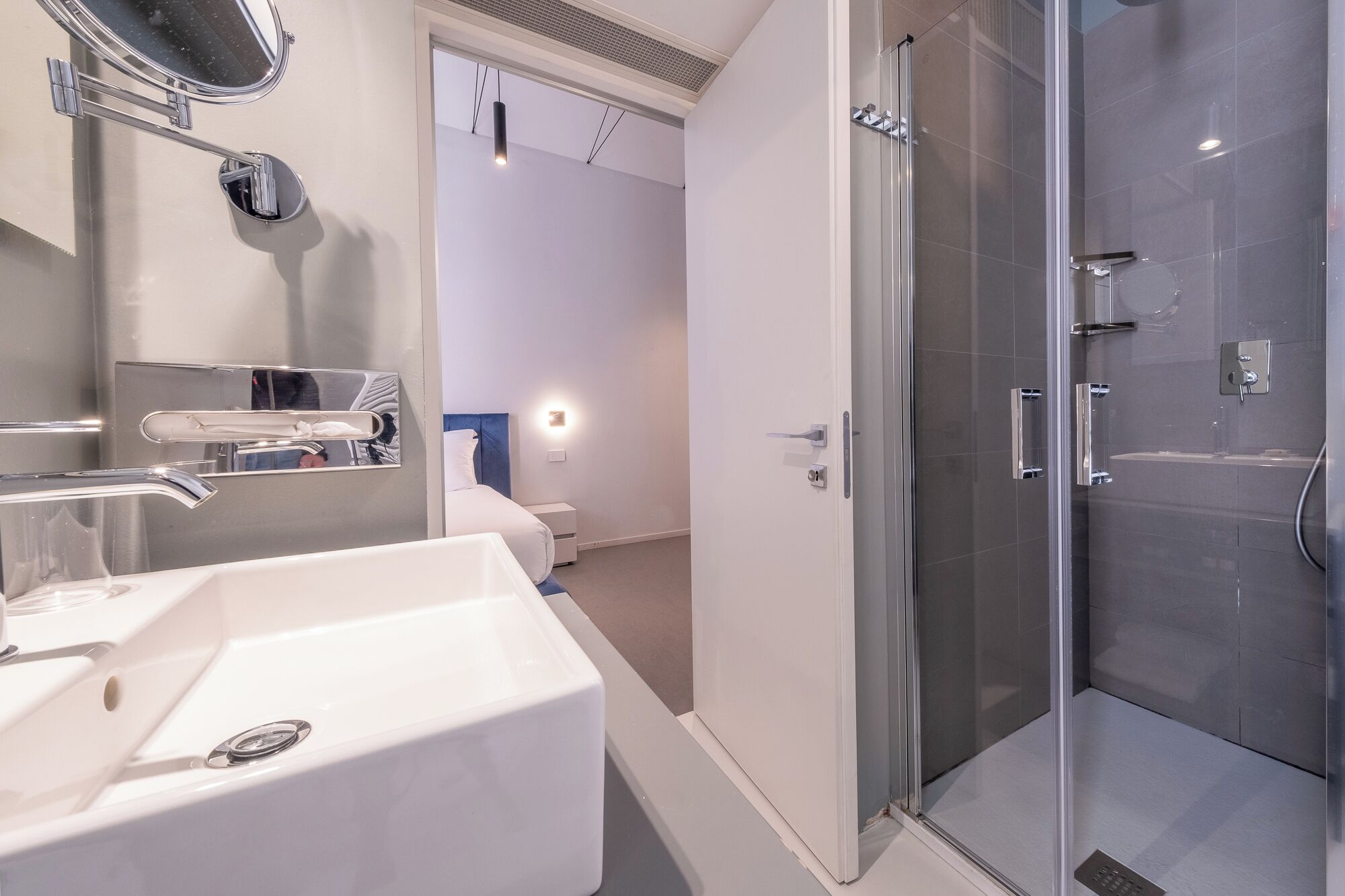 Une salle de bain moderne avec une douche à parois de verre, un lavabo blanc avec un miroir et une table de chevet avec une lampe.