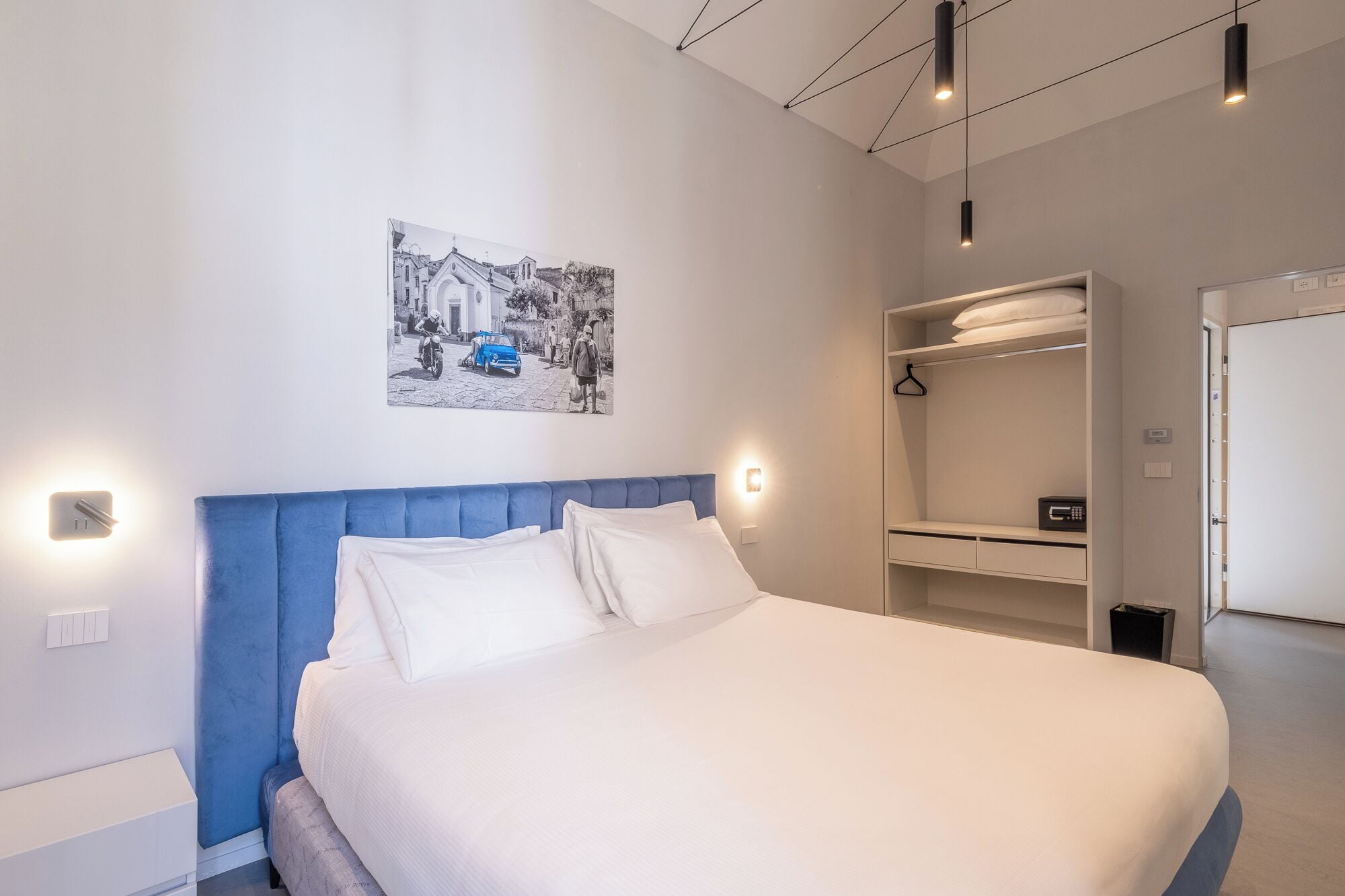 Un dormitorio con una cama grande, cabecera azul, luz empotrada en la pared, perchero y armario.