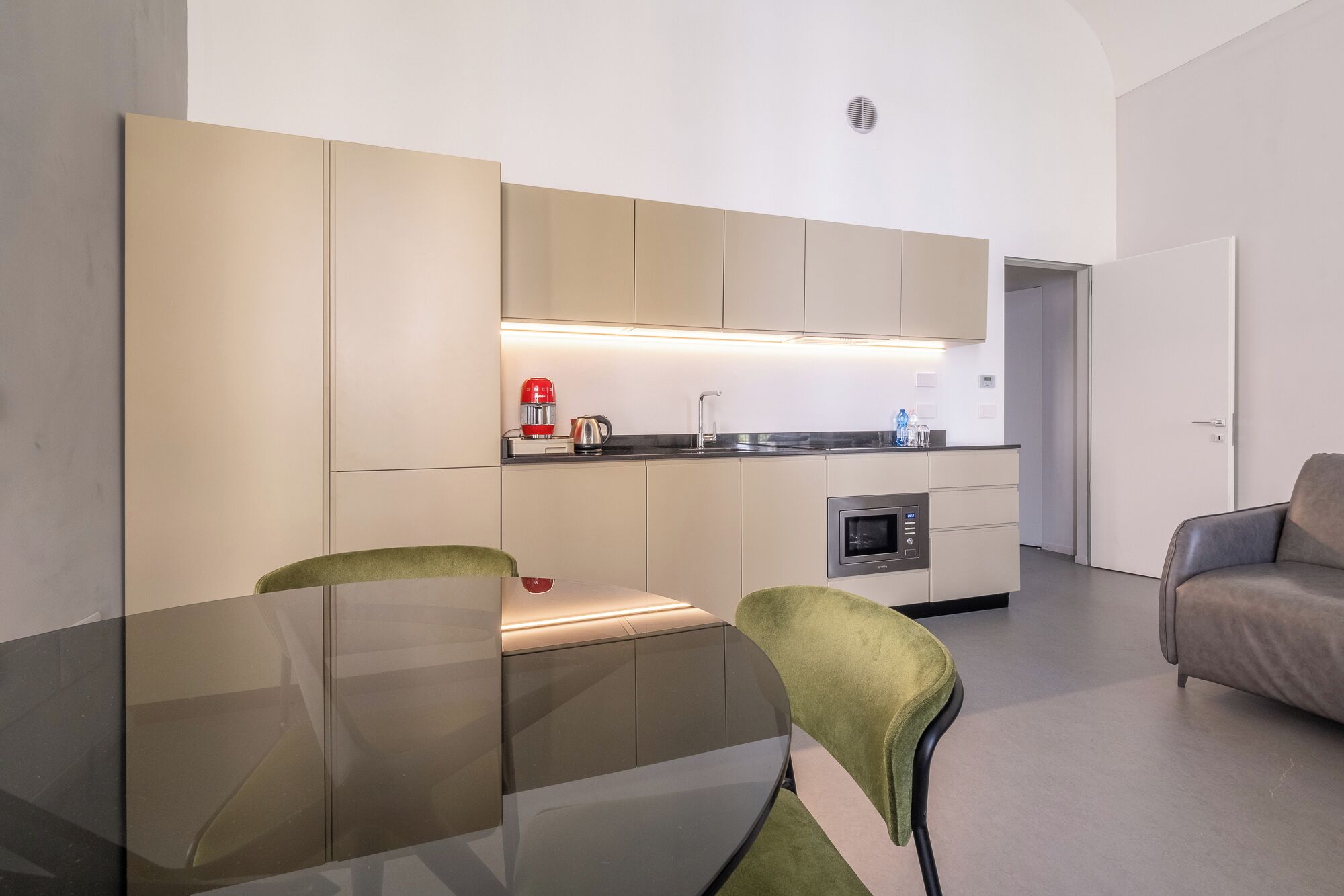 Una cocina moderna con horno integrado, cafetera y microondas. Hay una mesa de comedor con sillas y un sofá en la sala de estar.