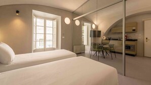 Un dormitorio moderno con dos camas, un separador de vidrio, un comedor y una kitchenette.