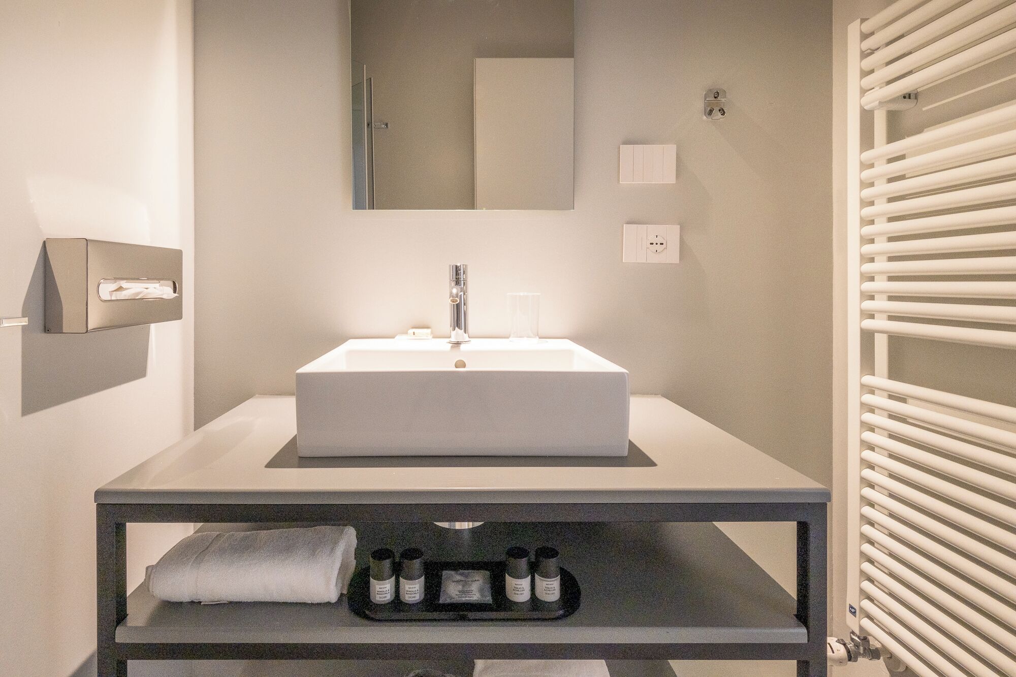 A modern bathroom with a large rectangular sink, a mirror above it, and a towel rack to the right.