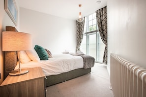 A bedroom with a bed, bedside lamp, and a window with curtains. - Windsor Castle Apartments (Windsor)