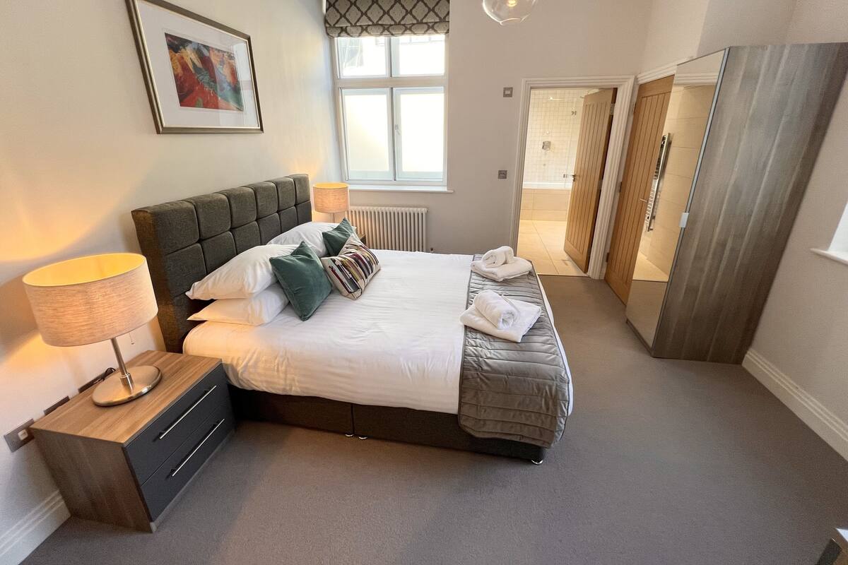 A neatly arranged bedroom with a bed, bedside lamp, and a framed picture on the wall.