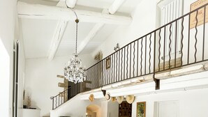 Een ruime eetruimte met een lange houten tafel en stoelen, een kroonluchter en een trap met ijzeren balustrade die naar een hoger niveau leidt.