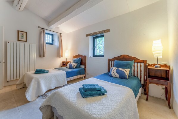 A bedroom with two beds, a radiator, a window with curtains, a bedside table with a lamp, and a picture on the wall. - Les Mas Ferrando Luberon: Beautiful authentic Mas Courroussouvo in Oppède-le-Vieux (Oppède)