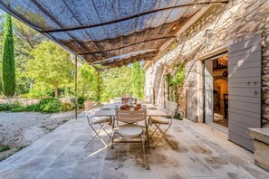 Un patio al aire libre con suelo de piedra, una mesa lista para comer y una zona de estar cubierta.