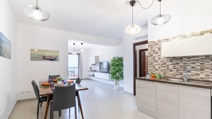 A modern kitchen with a tiled backsplash, a dining area with a table and chairs, and a hallway leading to a living space.