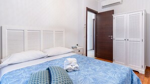 A bedroom with a bed, white headboard, white wardrobe, and a door leading to another room.