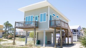Una casa frente al mar de dos pisos con un balcón en el nivel superior y un espacio cubierto en la planta baja.