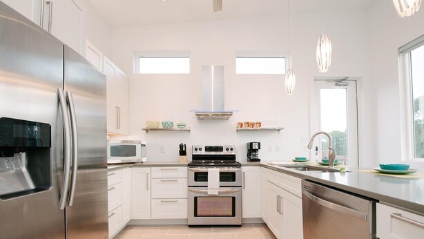 Una cocina moderna con electrodomésticos de acero inoxidable, armarios blancos y suelo de baldosas.