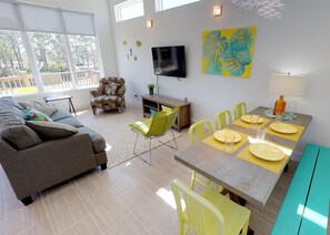 Un salon moderne avec un canapé, une table à manger pour quatre personnes et un téléviseur fixé au mur.
