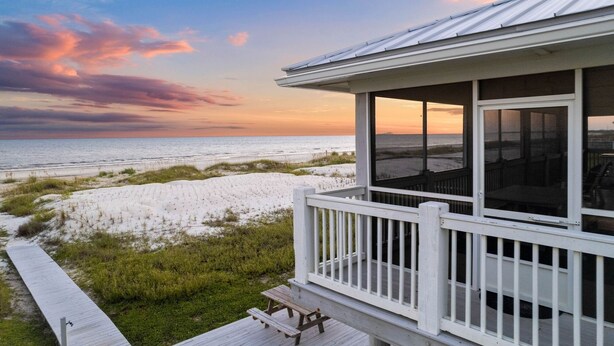 A beach house with a deck overlooking the ocean, featuring a large window and a view of the beach and dunes. - Gulffront w/ Screened Porch | Dogs Allowed (Indian Pass)
