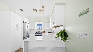 A modern kitchen with white cabinetry, a stainless steel refrigerator, a built-in oven, and a large island with bar stools. - Gulffront w/ Screened Porch | Dogs Allowed (Indian Pass)