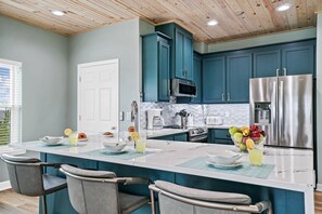 Une cuisine moderne avec des armoires de couleur turquoise, des appareils en acier inoxydable et un îlot central doté de tabourets de bar.