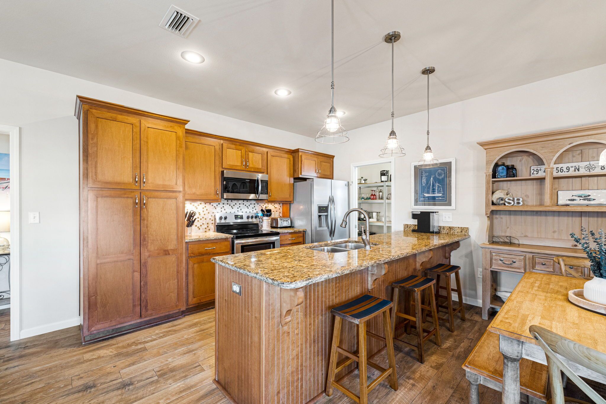 A modern kitchen with wooden cabinets, granite countertops, stainless steel appliances, and a central island with bar stools.