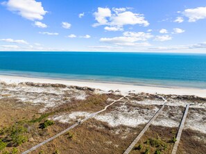 A beach with a wooden boardwalk leading to the water, sandy dunes, and a clear blue sky. - Pet-Friendly Cape San Blas Escape w/Pool (Cape San Blas)