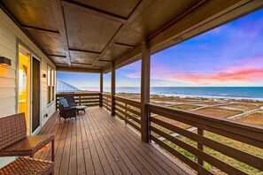 A wooden deck with wicker furniture overlooking a beach with a colorful sunset sky. - Pet-Friendly Beachfront Escape (Cape San Blas)