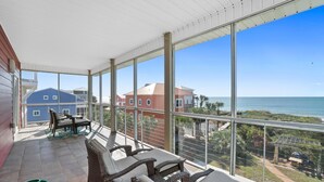 Ein überdachter Balkon mit Korbmöbeln und Blick aufs Meer.